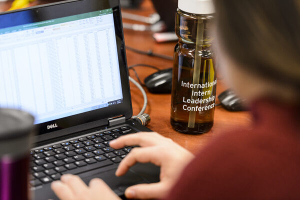 A photo shows hands typing into an Excel document on a laptop.